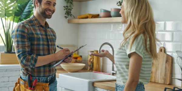 Beautiful young woman talking to male plumber while standing at the kitchen