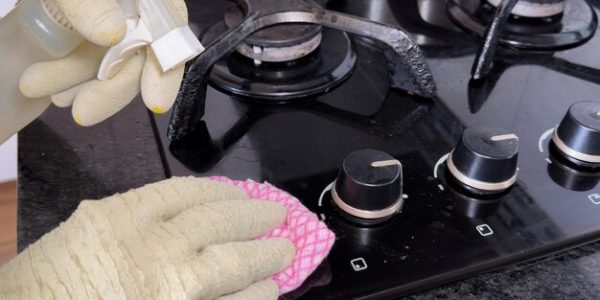 person-cleaning-modern-black-gas-stove-with-pink-cloth-spray-cleaner-eliminate-fat_597321-1121